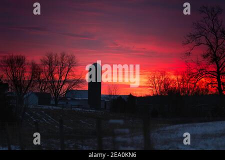 Ein Sonnenaufgangshimmel über einer kleinen Indiana Farm. Der Himmel besteht aus Rot, Gelb, Violett, Orangen und Blau. Ein Silo ist prominent gekennzeichnet. Stockfoto