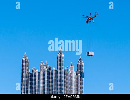 Ein Sky-Kran-Hubschrauber liefert eine Klimaanlage an die Spitze des PPG-Gebäudes in der Innenstadt von Pittsburgh, Pennsylvania, USA Stockfoto