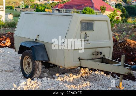 Es ist früh am Morgen bei Sonnenaufgang auf einem Straßenbauplatz, wo es einen geparkten Kompressor auf der marmorierten Straße neben einem neu gegrabenen Graben. Stockfoto