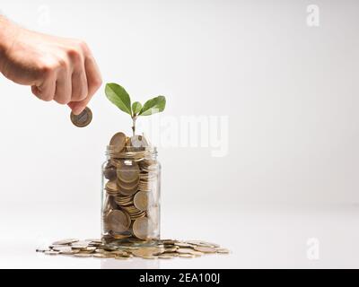 Hand der Person, die Münze hält, um in Glas zu setzen. Türkische Münzen in Gläsern. Pflanzen in Glas und türkische 1 TL Münzen Spar-und Finanzkonzept. Stockfoto