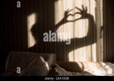 Frau macht Herzschatten mit ihren Händen an der Wand. Welt Tag der psychischen Gesundheit, Hoffnung und Liebe. Valentinstag 14 Februar Stockfoto