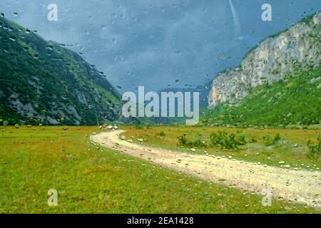 Regentropfen auf einem Autoglas, jenseits einer verschwommenen Sicht auf die unbefestigte Straße im Komarnica Canyon, Montenegro Stockfoto