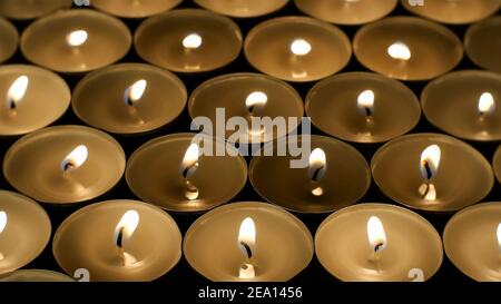 Viele brennende runde kleine Kerzen mit Reflexen brennen im Dunkeln. Feuerhintergrund. Selektiver Fokus. Nahaufnahme. Stockfoto