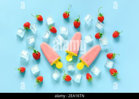 Hausgemachte Eiszapfen. Natürliches Eis in hellen Plastikformen, Erdbeeren und Eiswürfel auf blauem Hintergrund. Draufsicht Flat Lay. Stockfoto