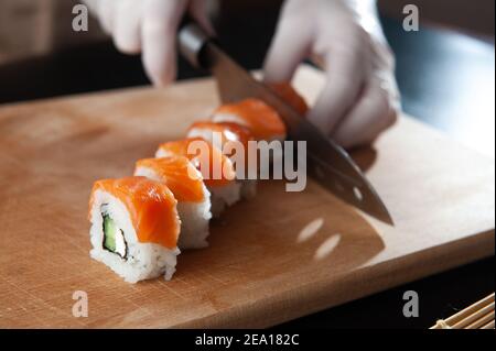 Nahaufnahme des Prozesses der Zubereitung von rollendem Sushi. Zubereitung des Sushi mit Sauce und Sesam, gießt köstliche frische Brötchen mit einer Sauce. Dunkler Rücken Stockfoto