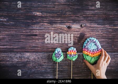 Kinder Hand nehmen eine bunte süße hausgemachte Baisaugen in Form von Eiern auf Holz Hintergrund. Flach liegend. Draufsicht. Viele süße Zephyren. Trendiger Blick von oben Stockfoto