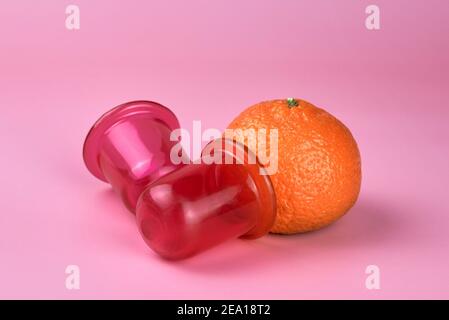 Zwei Massagegläser aus Silikon und eine Mandarine auf rosa Hintergrund, Anti-Cellulite und therapeutische Massageprodukte. Stockfoto