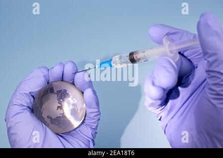 Die Hände der Frau in medizinischen Handschuhen halten einen Planeten Erde Globus und eine Spritze, das Konzept der Impfung. Stockfoto