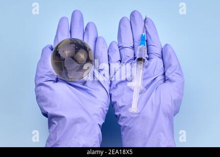 Die Hände der Frau in medizinischen Handschuhen halten einen Planeten Erde Globus und eine Spritze, das Konzept der Impfung. Stockfoto