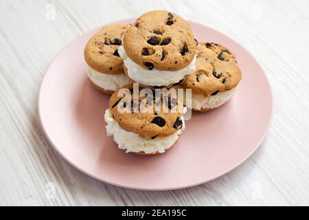Hausgemachte Schokolade Chip Cookie Ice Cream Sandwich auf einem rosa Teller auf einem weißen Holztisch, Seitenansicht. Stockfoto