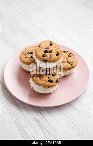 Hausgemachte Schokolade Chip Cookie Ice Cream Sandwich auf einem rosa Teller auf einem weißen Holzhintergrund, Seitenansicht. Stockfoto