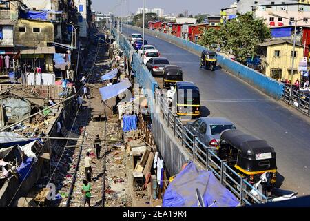 Mumbai, Maharashtra, Indien - Dezember 2016: Geparkte Tuk Tuks und Autos auf der Straßenbrücke entlang der Eisenbahnstraße in der Nähe von schmutzigen Slums und Wohnhäusern Stockfoto