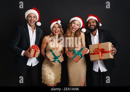 Porträt einer fröhlichen jungen multirassischen Gruppe von Freunden feiern zusammen Silvester isoliert auf schwarzem Hintergrund, hält Geschenke Stockfoto