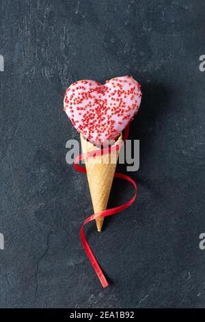 Herzförmiger Donut in einem Eiswaffelkegel auf schwarzem Hintergrund. Kreatives Backen für die st. Valentinstag. Stockfoto