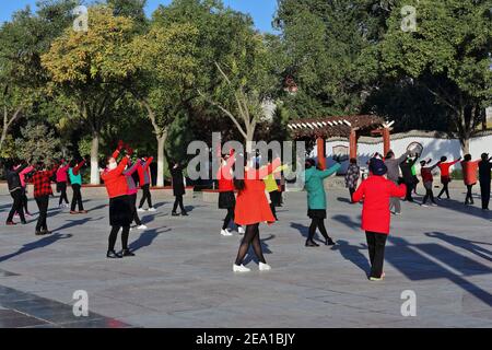 Maskierte Gruppentänzer in der frühen Morgensonne führen Gymnastik durch Choreografien zum Klang tragbarer Musik wie zu Halten Sie ihre körperliche Fitness Stockfoto