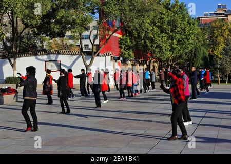 Maskierte Gruppentänzer in der frühen Morgensonne führen Gymnastik durch Choreografien zum Klang tragbarer Musik wie zu Halten Sie ihre körperliche Fitness Stockfoto