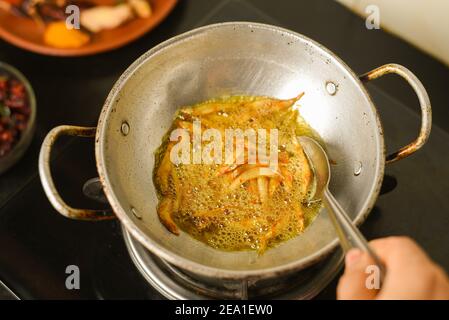 Draufsicht würzige heiße Sardellen Kerala Fisch Curry. Indisches Essen. Frau Hand machen Fisch braten mit roten Chili, Curryblatt, Kokosmilch. Asiatische Küche Stockfoto