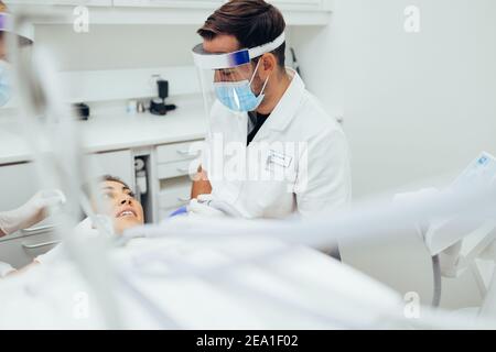Zahnarzt Behandlung einer weiblichen Patientin in der Zahnklinik. Männliche Arzt trägt Maske und Gesichtsschutz Behandlung mit Patienten in der Zahnklinik diskutieren. Stockfoto