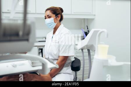 Frau Arzt trägt Gesichtsmaske sitzt in der Klinik und Untersuchung Patient. Zahnärztin sitzt auf einem Stuhl und überprüft einen Patienten. Stockfoto