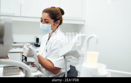 Zahnarzt, der eine zahnärztliche Behandlung in den Zähnen eines Patienten mit Werkzeugen. Weibliche Zahnärztin trägt Gesichtsmaske arbeiten in ihrer Klinik. Stockfoto