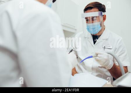 Männlicher Arzt, der an den Zähnen des Patienten arbeitet, mit einem Assistenten vor dem Patienten. Zahnarzt Behandlung von Patienten in seiner Klinik. Stockfoto