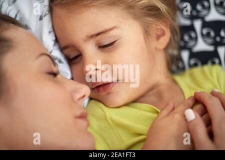 Eine kleine Tochter im sorglosen Schlaf mit ihrer Mam am Morgen. Familie, Zuhause, zusammen Stockfoto