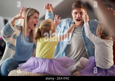 Junge Eltern imitieren Monster mit ihren kleinen Töchtern in fröhlicher Atmosphäre zu Hause. Familie, zu Hause, spielen Stockfoto