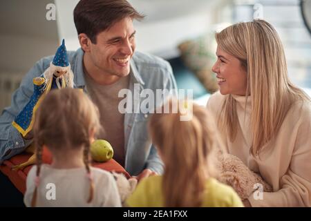 Mama und kleine Töchter genießen Dad Leistung mit einer Puppe in einer fröhlichen Atmosphäre zu Hause. Familie, zu Hause, spielen Stockfoto