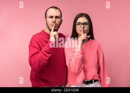 Foto von süßen Paar in Gläsern steht und zeigt shhh. Männchen und Weibchen sehen ernst und streng aus, isoliert auf rosa Hintergrund Stockfoto