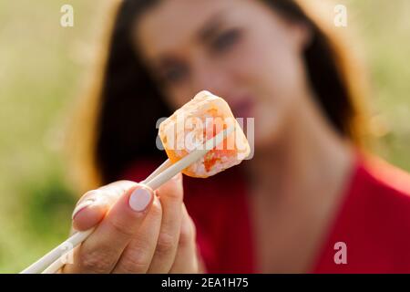 Nahaufnahme eines Sushi. Attraktive Mädchen hält Sushi mit Essstäbchen in den Händen und gibt Ihnen. Kurier lieferte Sushi-Set für hübsche Frau. Black Box mit Stockfoto