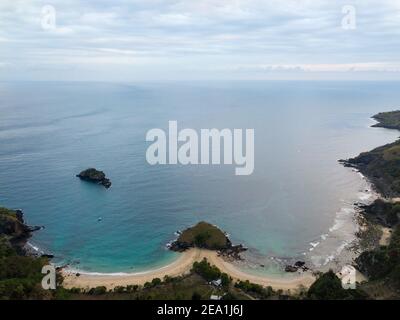 Drohnenblick auf eine abgeschiedene tropische Bucht mit türkisfarbenem Wasser, weißem Sandstrand und grünen bewaldeten Landzungen in Nusa Penida, Bali, Indonesien. Stockfoto