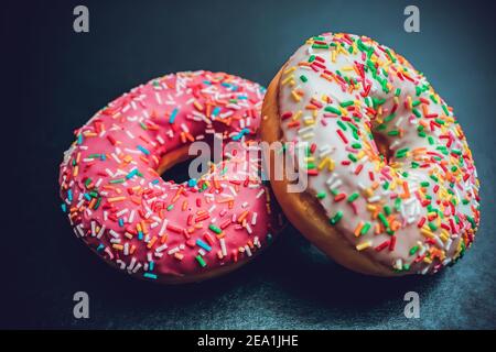 Frische, leckere und süße Donuts mit verschiedenen Glasuren und verschiedenen Füllungen auf dunklem Grund Stockfoto