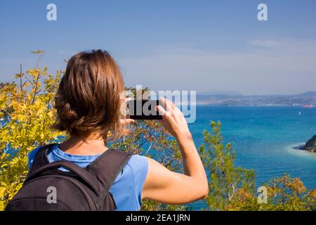 Eine Wanderin mit einem Backpacker, der mit ihrem Smartphone ein Foto vom Meer gemacht hat. Strunjan, Slowenien Stockfoto
