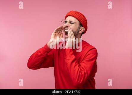 Foto von attraktiven Mann mit Bart in Brille und rote Kleidung. Männliche Schreie und Schreie, isoliert auf rosa Hintergrund Stockfoto