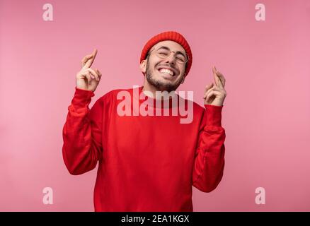 Foto von attraktiven Mann mit Bart in Brille und rote Kleidung. Männlich gekreuzte Daumen und lächelt, isoliert auf rosa Hintergrund Stockfoto