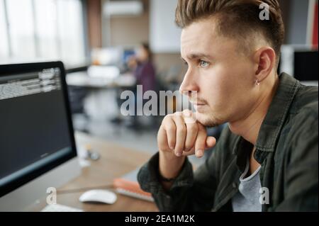 Nachdenklicher männlicher IT-Spezialist sitzt am Tisch Stockfoto