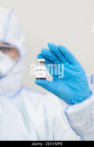 Medic in Hazmat Anzug, Handschuhe, Maske und Schutzbrille hält Impfstoff gegen covid-19 Stockfoto