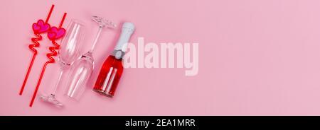 Zwei Sektgläser mit roten Plastiktrinkstrohhalmen mit Herzen und roter Sektflasche auf rosa Hintergrund. Stockfoto