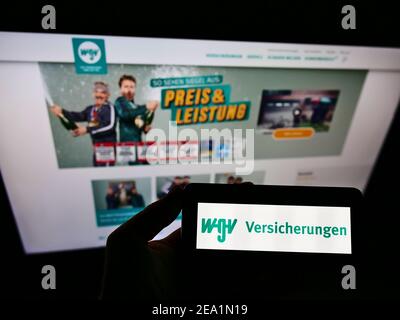 Person, die Mobiltelefon mit Logo der WGV Versicherungen auf dem Bildschirm vor der Webseite hält. Fokus auf Handy-Display. Stockfoto