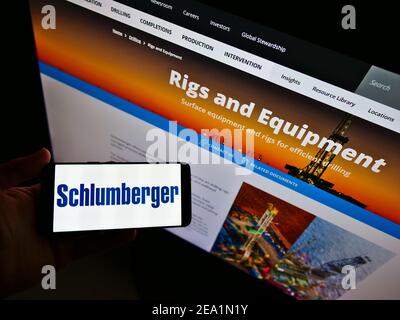 Person, die Smartphone mit Firmenlogo des oilfield-Dienstleistungsunternehmens Schlumberger auf dem Bildschirm vor der Website hält. Konzentrieren Sie sich auf die Telefonanzeige. Stockfoto