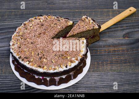 Schokoladenkuchen mit geriebener Schokolade mit Walnüssen und einem geschnittenen Stück auf einem Bambusspatel mit Fruchtfüllung auf einem hölzernen Vintage-Hintergrund verziert. Der Stockfoto