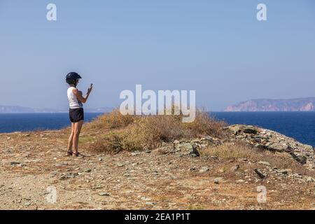 Folegandros Island, Griechenland - 25. September 2020: Frau im schwarzen Helm, die ein Foto macht. Küste Ägäis. Stockfoto