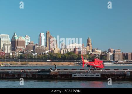 Roter Hubschrauber mit Touristen in Heliport in New York. USA. Hubschrauber auf dem Hintergrund Fluss und New York und Gebäude von Brooklyn. Stockfoto