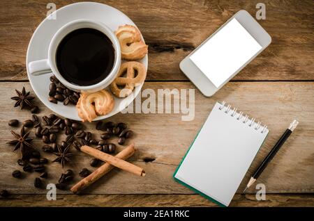 Kaffee-Kekse und Smartphone-Notebook auf einem Holztisch am Morgen. Stockfoto