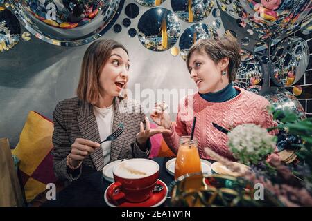 Lustige Mädchen plaudern und füttern sich gegenseitig Süßigkeiten über ein Kaffeepause in einem Restaurant Stockfoto