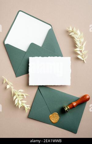 Vintage grüne Umschläge mit Wachs Siegel Stempel, unbeschriftete Papierkarte, getrocknete Blumen auf Paste beige Hintergrund. Retro-Stil Hochzeit Einladung mockup, Begrütin Stockfoto