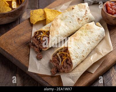 Burritos mit Hackfleisch, gebratenen Bohnen und Käse auf einem Holzschneidebrett Stockfoto