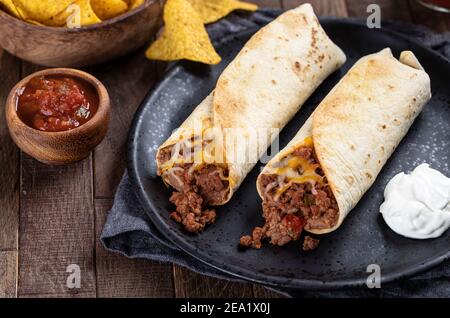 Burritos mit Hackfleisch, gebratenen Bohnen und Käse auf einem schwarzen Teller mit Salsa und Tortilla-Chips Stockfoto