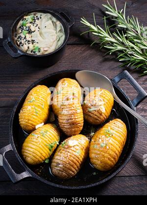 Gebackene Bratkartoffeln (gebackene Kartoffeln) in einer runden Pfanne aus schwarzem Gusseisen mit Knoblauch und Olivenöl, serviert mit einem Avocado-Dip Stockfoto