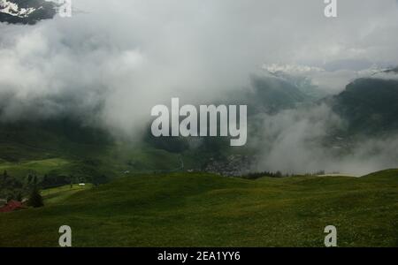 Zermatt umgeben von verschneiten Berggipfeln und hügeligen Wildblumenwiesen, die durch eine Wolkenpause gesehen werden. Stockfoto